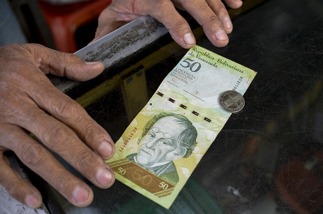 A man compares a new 50-Bolivar-coin with a Bolivar-note of the same denomination at a kiosk in Caracas on December 28, 2016. Venezuela took delivery on December 27 of its third load of new, bigger denomination banknotes, its central bank said, but there was no sign of them in circulation yet despite official promises and mounting public anxiety. Maduro's announcement that the 100-bolivar notes would suddenly no longer be legal tender provoked long lines of people trying to change them, and looting and rioting in some areas, resulting in four deaths. / AFP PHOTO / FEDERICO PARRA